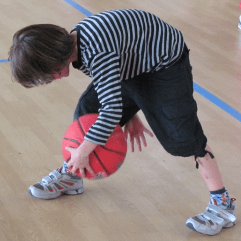 Boy executing basketball drill between knees on gym floor