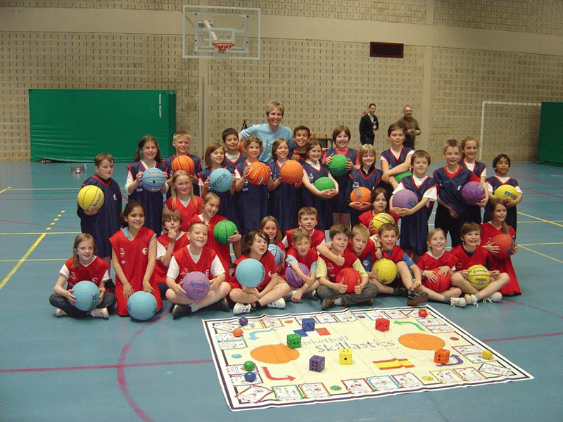 Skillastics CEO, Sandy Slade, surrounded by students holding basketballs In gym