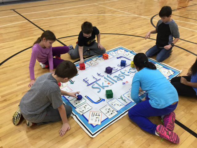 Students surrounding Oversize Fitness Skillastics Mat, rolling die