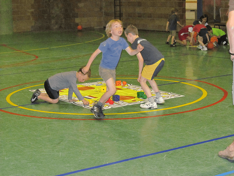 Child running to team from oversize mat in gymnasium.