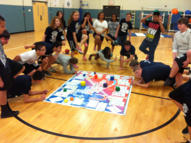 Secondar students surrounding Fitness Xtreme Skillastics Mat, smiling.