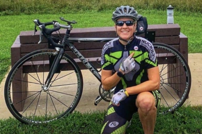 Jess Wadleigh kneeling on the ground next to a bicycle wearing safety gear.